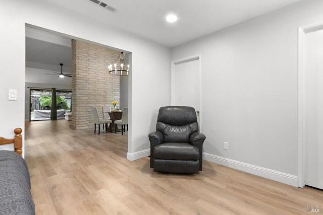 living area featuring ceiling fan with notable chandelier, ornate columns, and light wood-type flooring