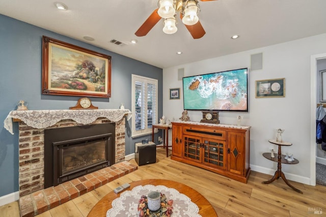 living room featuring ceiling fan, a brick fireplace, and light wood-type flooring