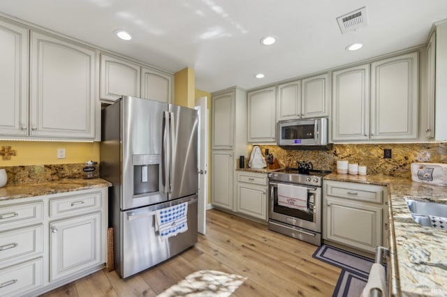 kitchen with sink, light stone counters, light wood-type flooring, stainless steel appliances, and decorative backsplash