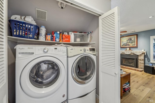 clothes washing area featuring hardwood / wood-style floors, a fireplace, and washing machine and dryer