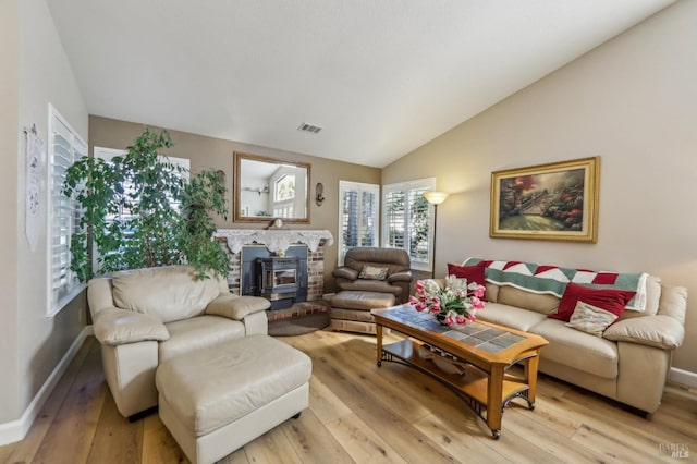 living room featuring vaulted ceiling, a wood stove, and light wood-type flooring