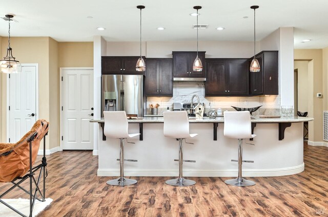 kitchen with premium range hood, backsplash, dark brown cabinets, light stone counters, and gas stove