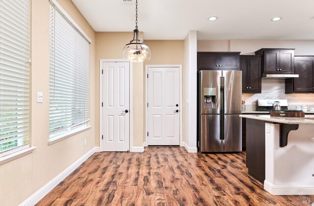 kitchen featuring pendant lighting, dark brown cabinetry, appliances with stainless steel finishes, and light stone countertops