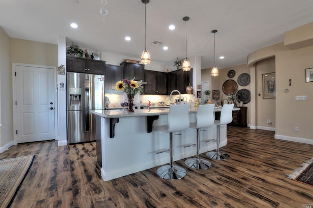 kitchen with pendant lighting, dark wood-type flooring, a kitchen breakfast bar, light stone countertops, and stainless steel fridge with ice dispenser