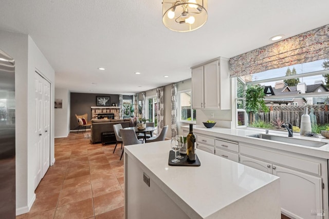 kitchen featuring light countertops, light tile patterned floors, a warm lit fireplace, white cabinetry, and a sink