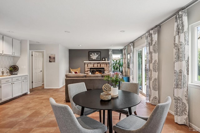 dining area with baseboards, a brick fireplace, and light tile patterned flooring