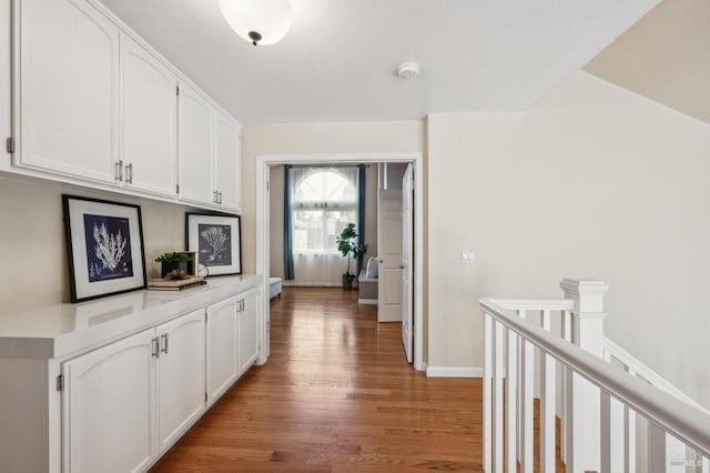 hallway featuring an upstairs landing, baseboards, and light wood finished floors