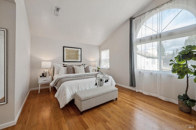 bedroom with visible vents, baseboards, light wood-style floors, and vaulted ceiling