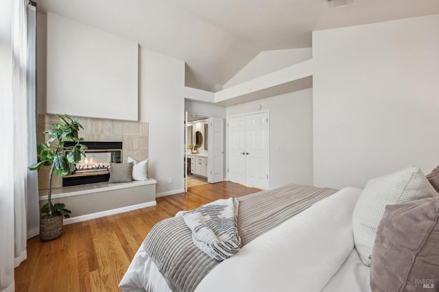 bedroom with wood finished floors, baseboards, a fireplace, vaulted ceiling, and connected bathroom