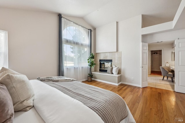 bedroom with light wood-type flooring, lofted ceiling, baseboards, and a tile fireplace