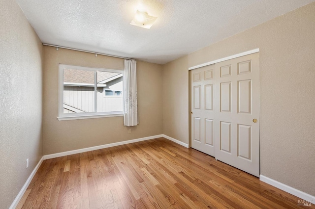 unfurnished bedroom with light wood-style flooring, baseboards, a closet, and a textured ceiling