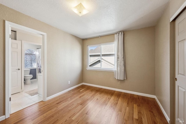 unfurnished bedroom featuring light wood-style floors, baseboards, and a textured ceiling