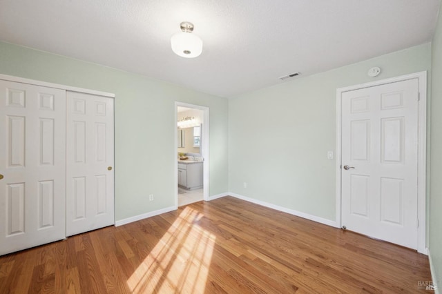 unfurnished bedroom featuring a closet, visible vents, light wood-type flooring, and baseboards