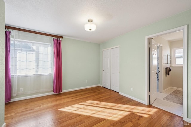 unfurnished bedroom featuring light wood-type flooring, baseboards, and ensuite bathroom