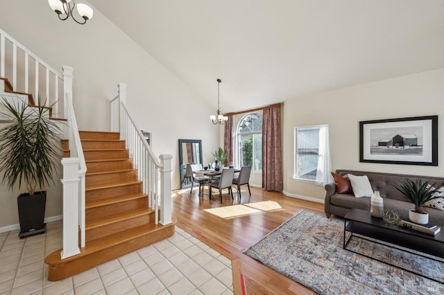 living area with baseboards, high vaulted ceiling, light wood-style flooring, stairs, and a chandelier