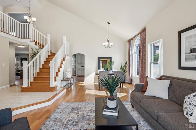 living area with high vaulted ceiling, wood finished floors, an inviting chandelier, baseboards, and stairs