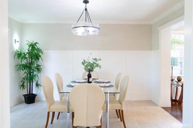 dining space with ornamental molding, wainscoting, a decorative wall, and an inviting chandelier