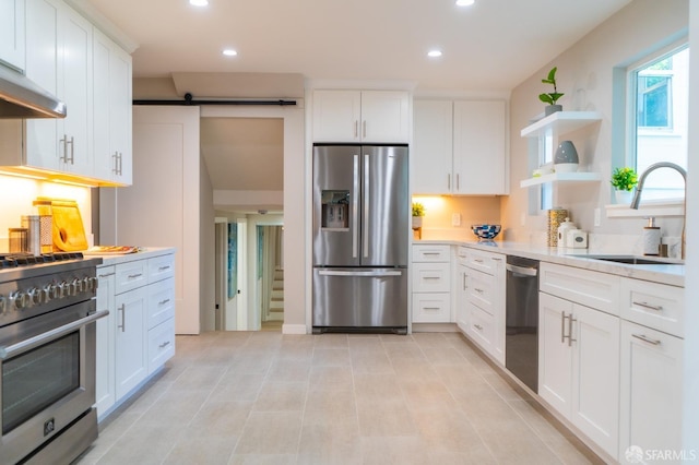 kitchen featuring open shelves, stainless steel appliances, a barn door, white cabinetry, and a sink