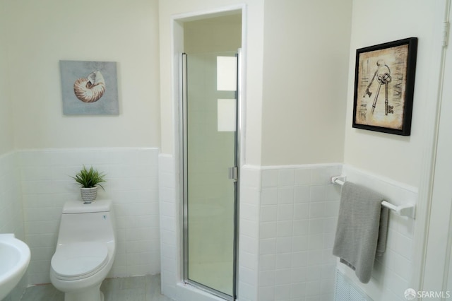 bathroom with toilet, a stall shower, tile walls, and wainscoting