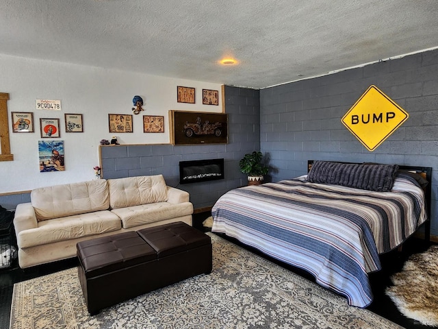 bedroom featuring concrete block wall, a glass covered fireplace, and a textured ceiling