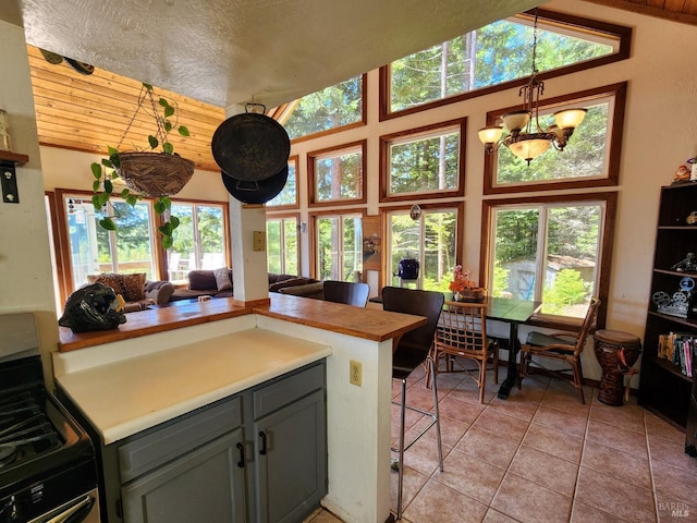 kitchen with a peninsula, gray cabinets, light countertops, stainless steel range with gas cooktop, and a chandelier