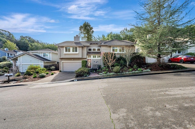 view of front of property featuring a garage, driveway, a tiled roof, a residential view, and a chimney