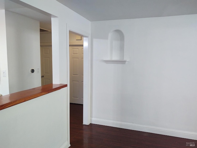 corridor featuring dark wood-type flooring and baseboards