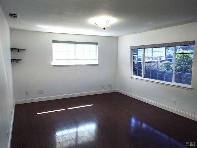 unfurnished room with dark wood-type flooring, visible vents, and baseboards