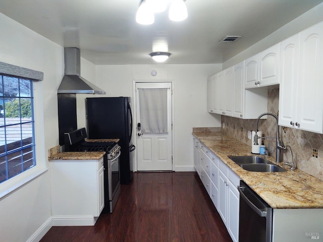 kitchen with dark wood finished floors, stainless steel appliances, white cabinets, a sink, and wall chimney range hood