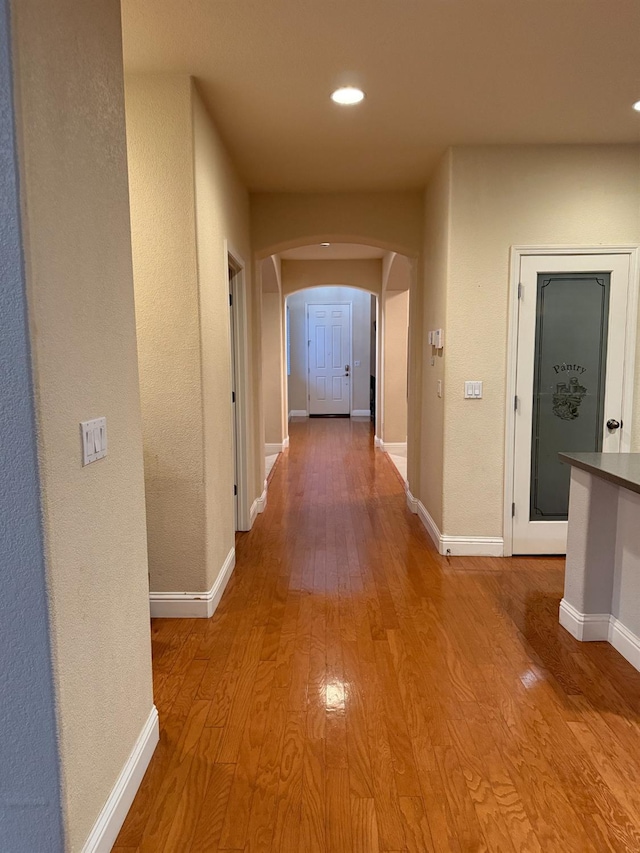 hallway featuring arched walkways, recessed lighting, baseboards, and wood finished floors