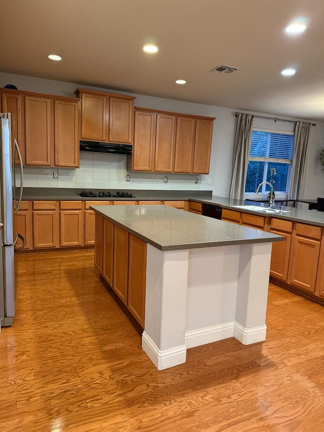 kitchen featuring a center island, light wood-style floors, a sink, ventilation hood, and black appliances