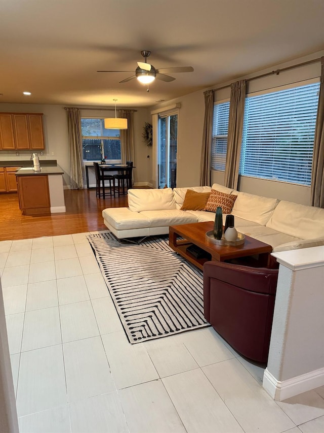 living area with light tile patterned flooring, ceiling fan, and baseboards