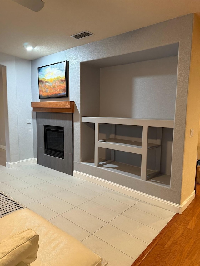 unfurnished living room with built in shelves, baseboards, visible vents, and a tiled fireplace