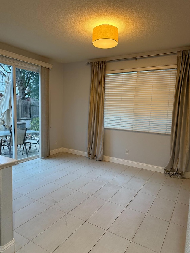 unfurnished room featuring baseboards, a textured ceiling, and light tile patterned flooring