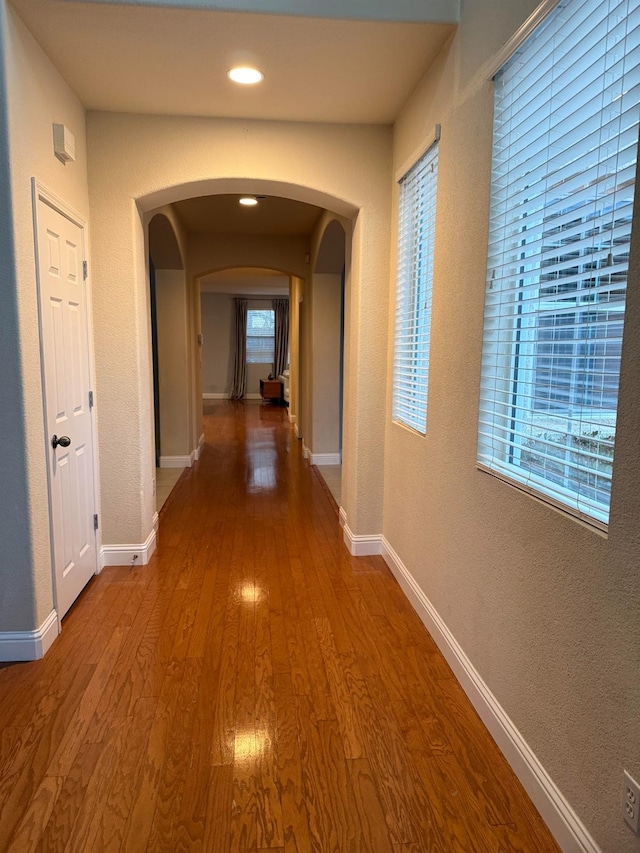 hall with arched walkways, a textured wall, wood finished floors, and baseboards