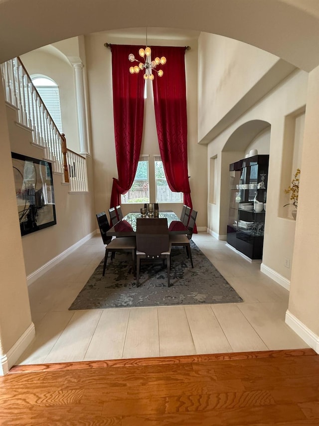 tiled dining area with a towering ceiling, an inviting chandelier, baseboards, and ornate columns