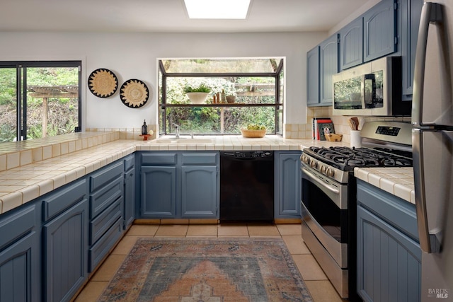 kitchen with stainless steel appliances, blue cabinetry, and tile countertops