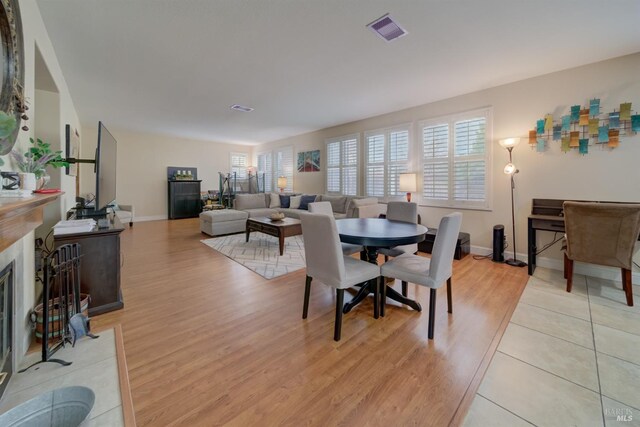 dining area featuring light wood-style floors, baseboards, visible vents, and a fireplace with flush hearth