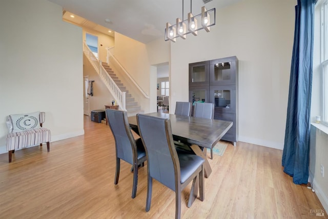 dining room with stairs, light wood-type flooring, a towering ceiling, and baseboards
