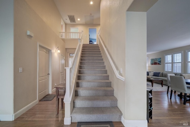 stairway with baseboards, visible vents, wood finished floors, a high ceiling, and recessed lighting
