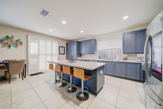 kitchen featuring light tile patterned floors, a breakfast bar area, visible vents, freestanding refrigerator, and a center island