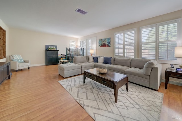 living area with a healthy amount of sunlight, light wood-style floors, baseboards, and visible vents