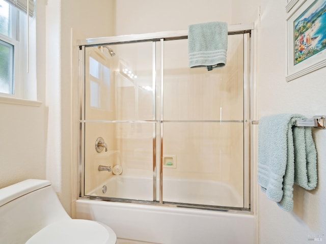 bathroom with bath / shower combo with glass door and toilet