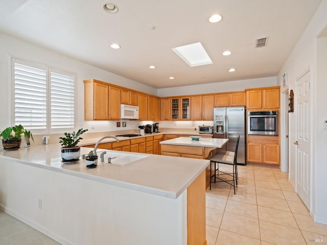 kitchen featuring sink, appliances with stainless steel finishes, a skylight, a center island, and a kitchen bar