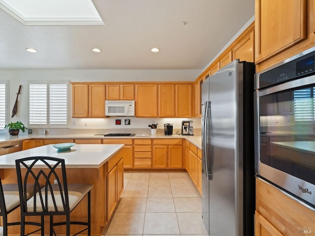 kitchen featuring a kitchen island, appliances with stainless steel finishes, light tile patterned floors, and a kitchen bar