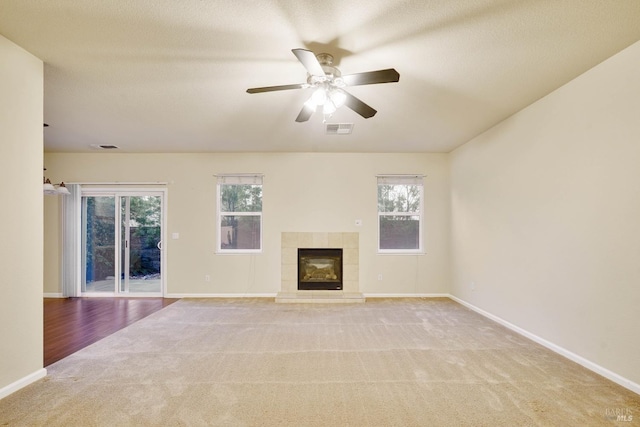 unfurnished living room with a tiled fireplace, plenty of natural light, light colored carpet, and ceiling fan