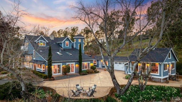 back house at dusk featuring a fire pit, a garage, and a patio