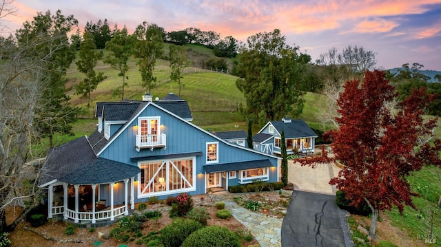 back house at dusk with a balcony and covered porch