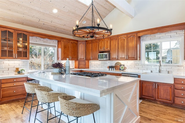 kitchen with brown cabinetry, appliances with stainless steel finishes, a center island, a sink, and backsplash