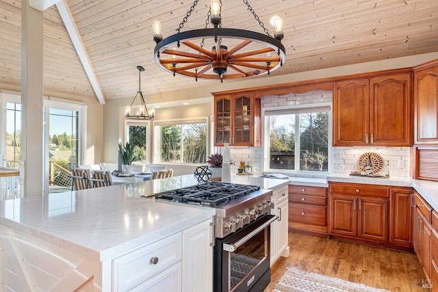 kitchen with a chandelier, light wood-style flooring, stainless steel stove, light countertops, and glass insert cabinets